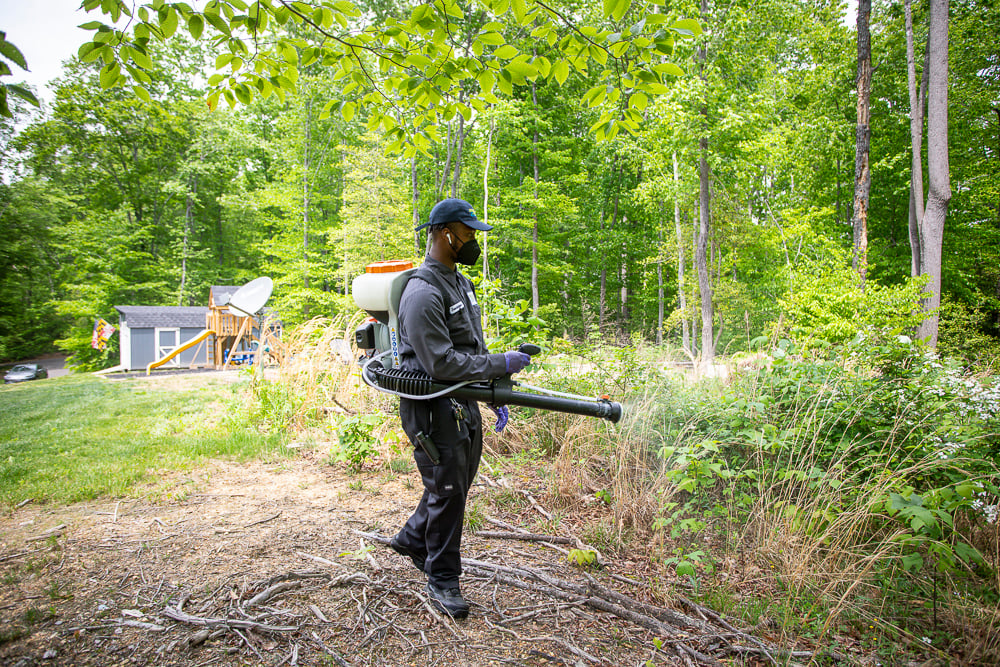 mosquito control technician sprays perimeter of property