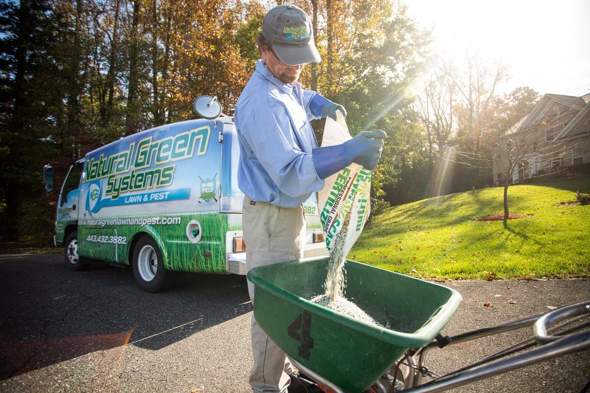 lawn care technician pours fertilizer into spreader