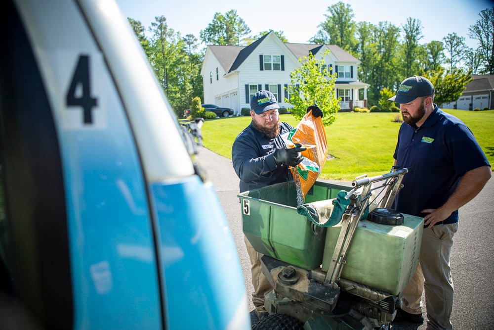 Lawn technicians pour fertilizer into ride on spreader